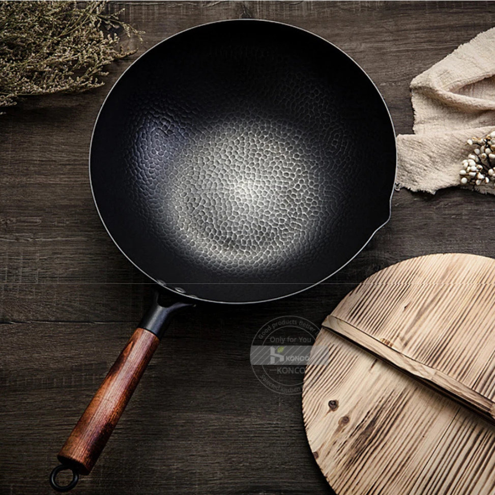 Black wok with wooden handle on a wooden surface next to a wooden lid