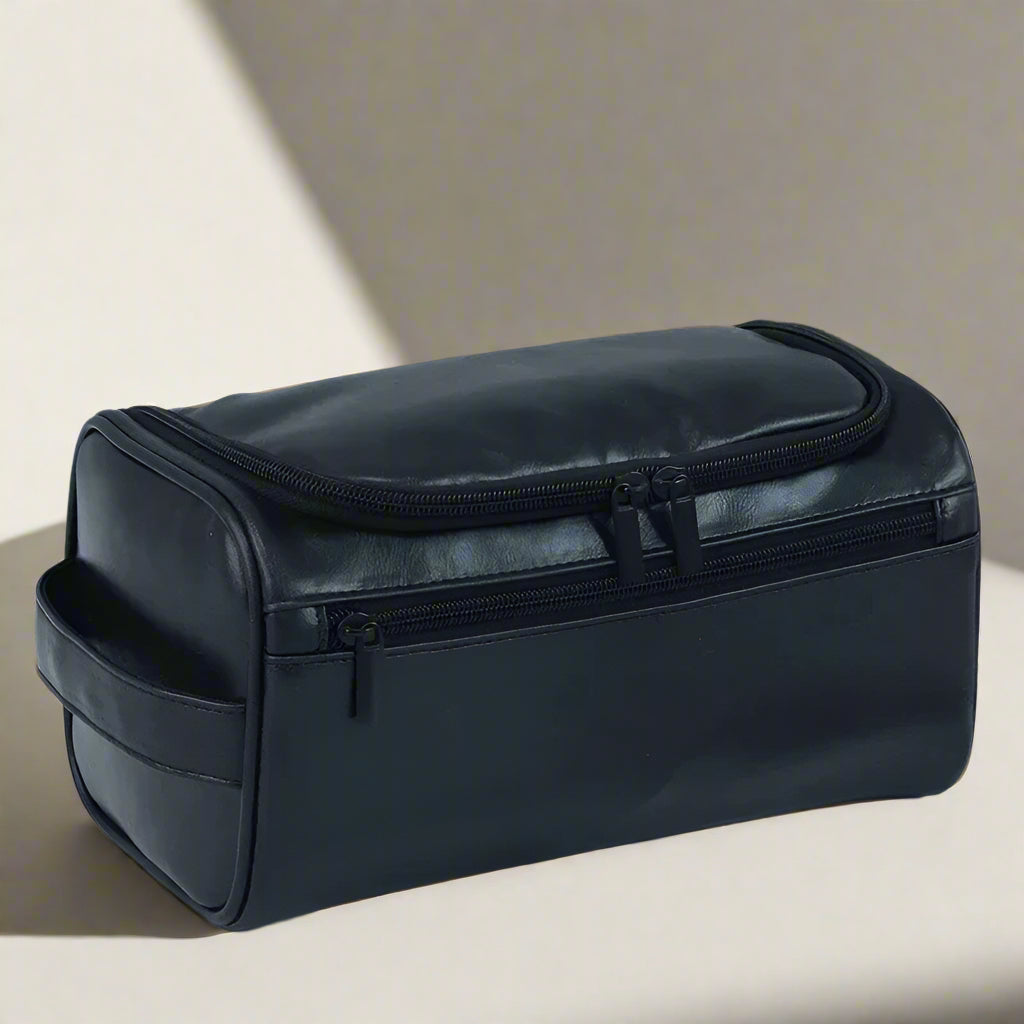 Black toiletry bag with dimensions displayed, placed on a light surface with grooming products.