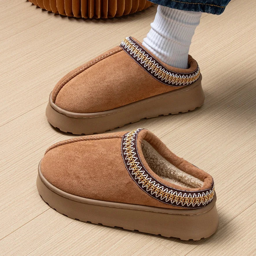 Brown slippers with decorative trim on a wooden floor.