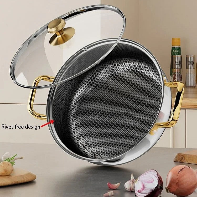 Stainless steel frying pan with gold handles and glass lid on a kitchen counter.