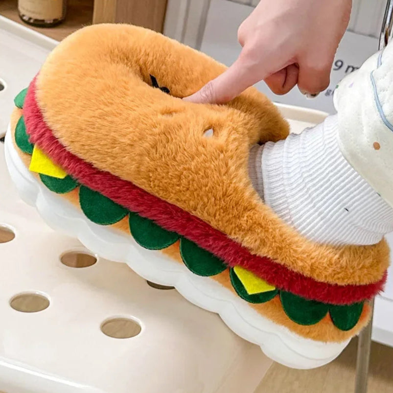 Hamburger-shaped slipper being worn with a hand pointing at it, on a chair.