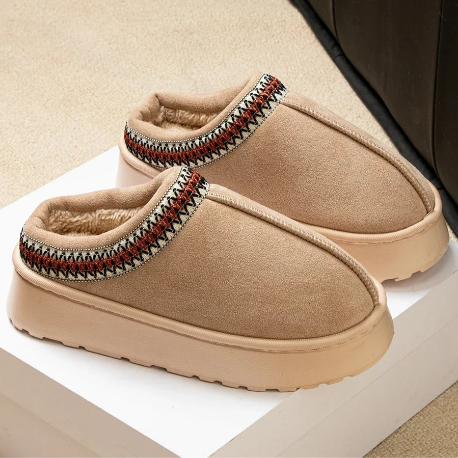 Pair of beige slippers with patterned straps on a white surface.