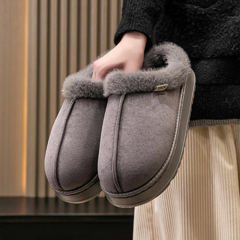 Person holding gray slippers with fur trim against a neutral background