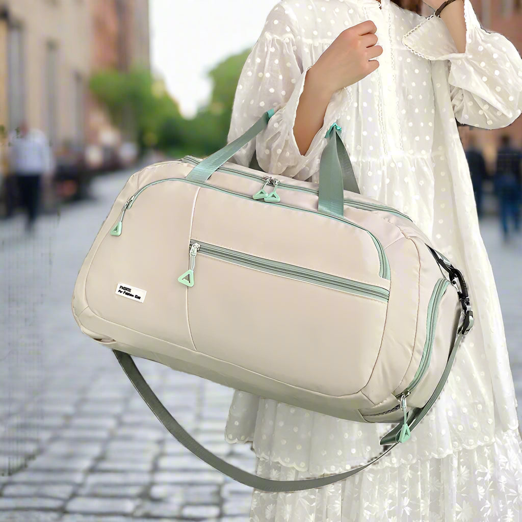 Person holding a beige duffel bag with green accents in a room setting.