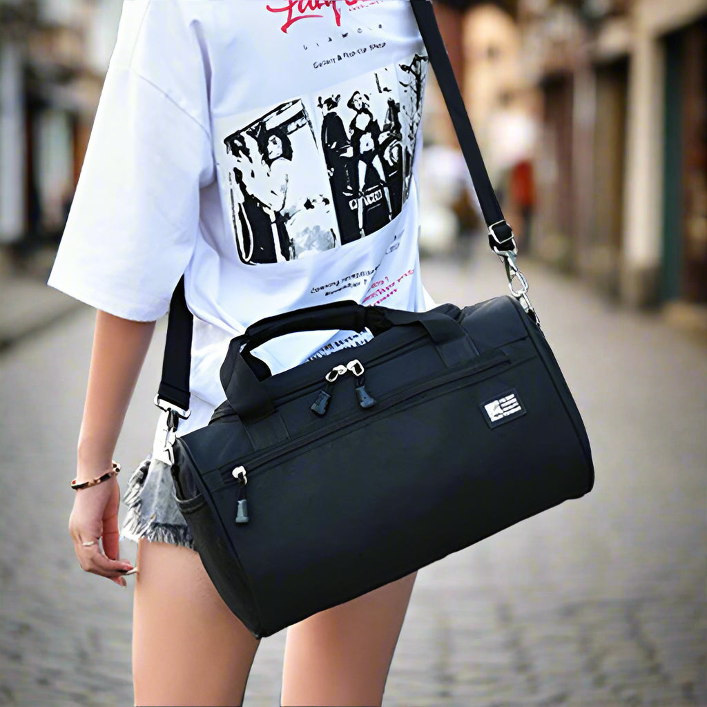 Person holding a black duffel bag in an outdoor setting