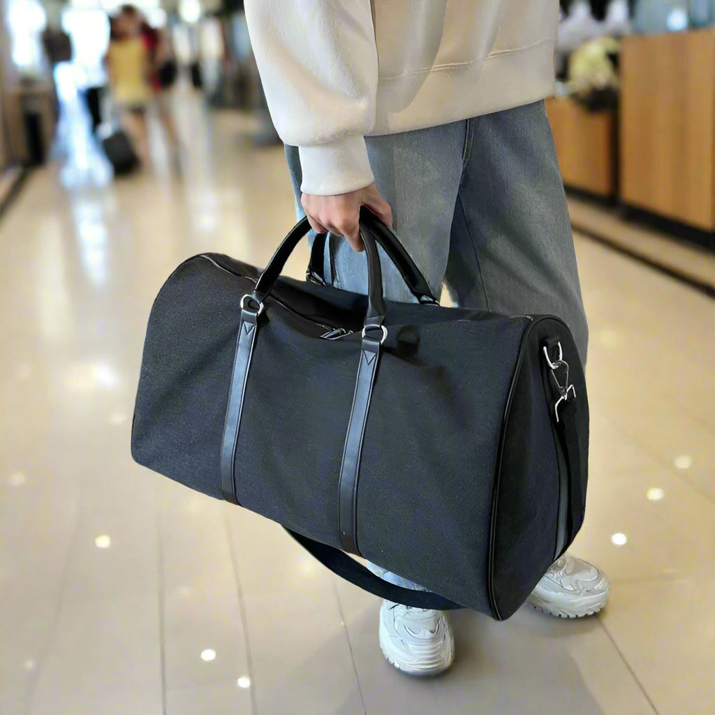 Person holding a black duffel bag indoors on a wooden floor.