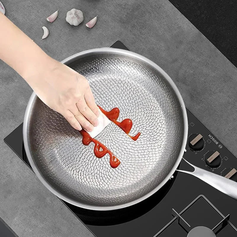 Person using a knife to spread red sauce on a non-stick frying pan on a stove.