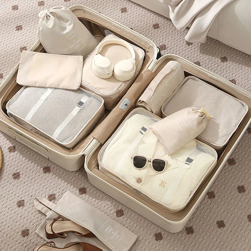 Open beige suitcase with organized packing including clothes, bags, and sunglasses on a patterned surface.