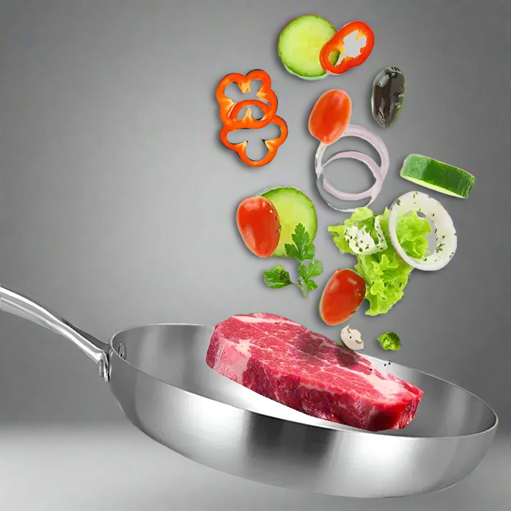 Stainless steel frying pan with raw steak and flying vegetables on a gray background, featuring the KEMORELA brand.