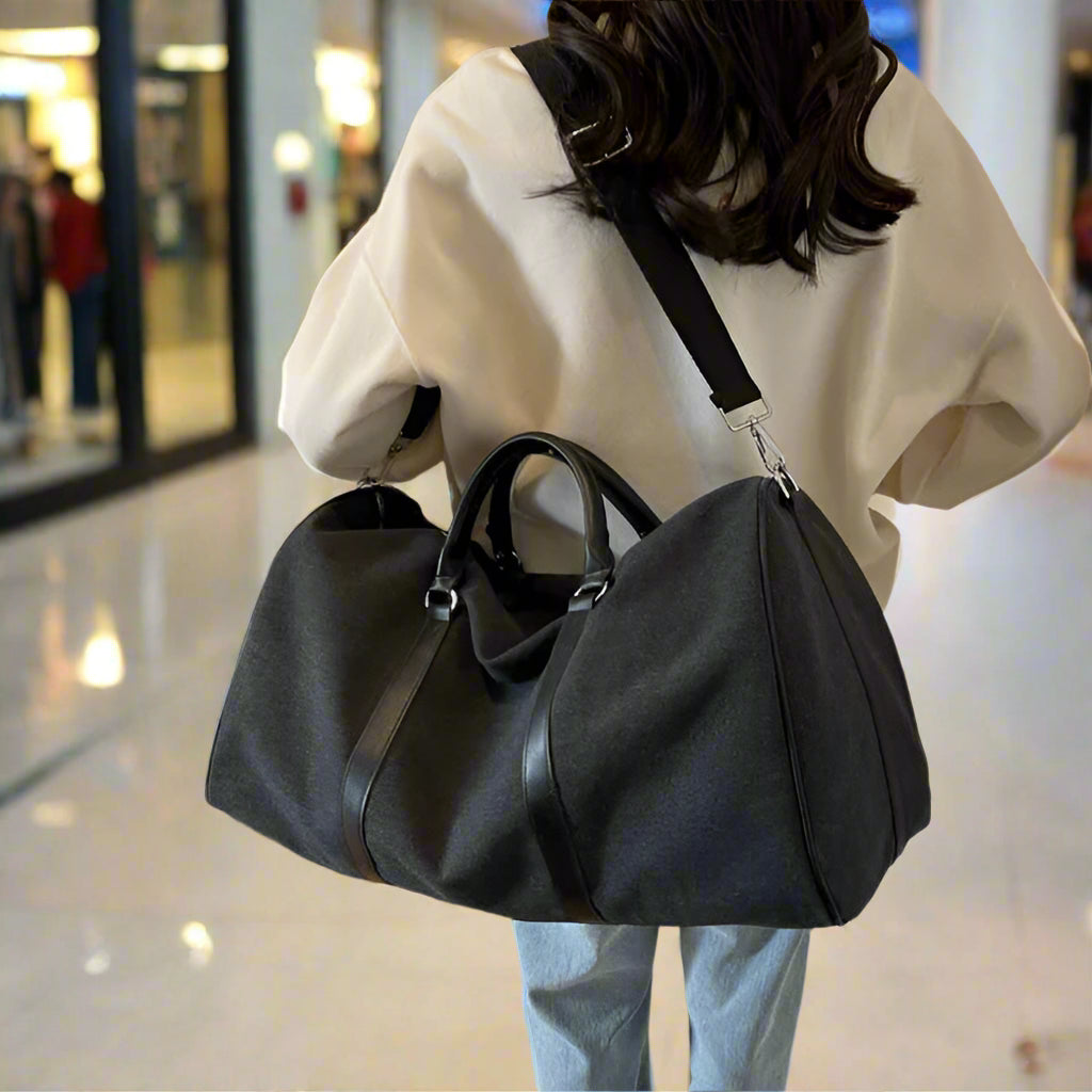 Person holding a black duffel bag in a room with wooden floor and beige wall.