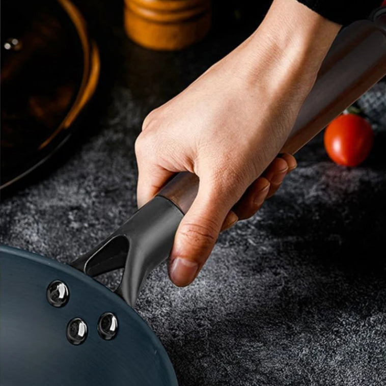 Hand holding a black frying pan on a dark surface with a blurred background