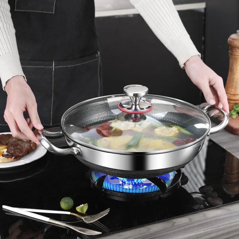 Stainless steel wok with glass lid on a stove, person holding it