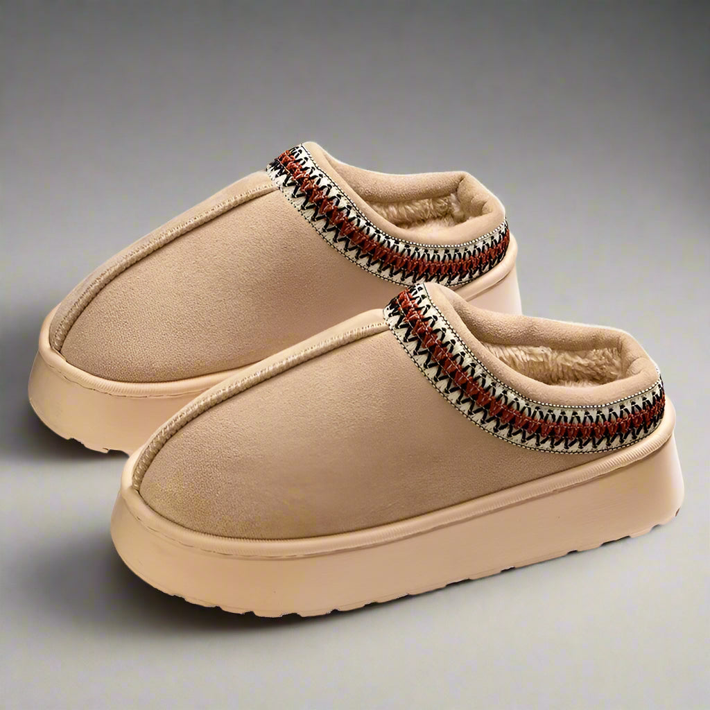 Pair of beige slippers with patterned trim on a white background