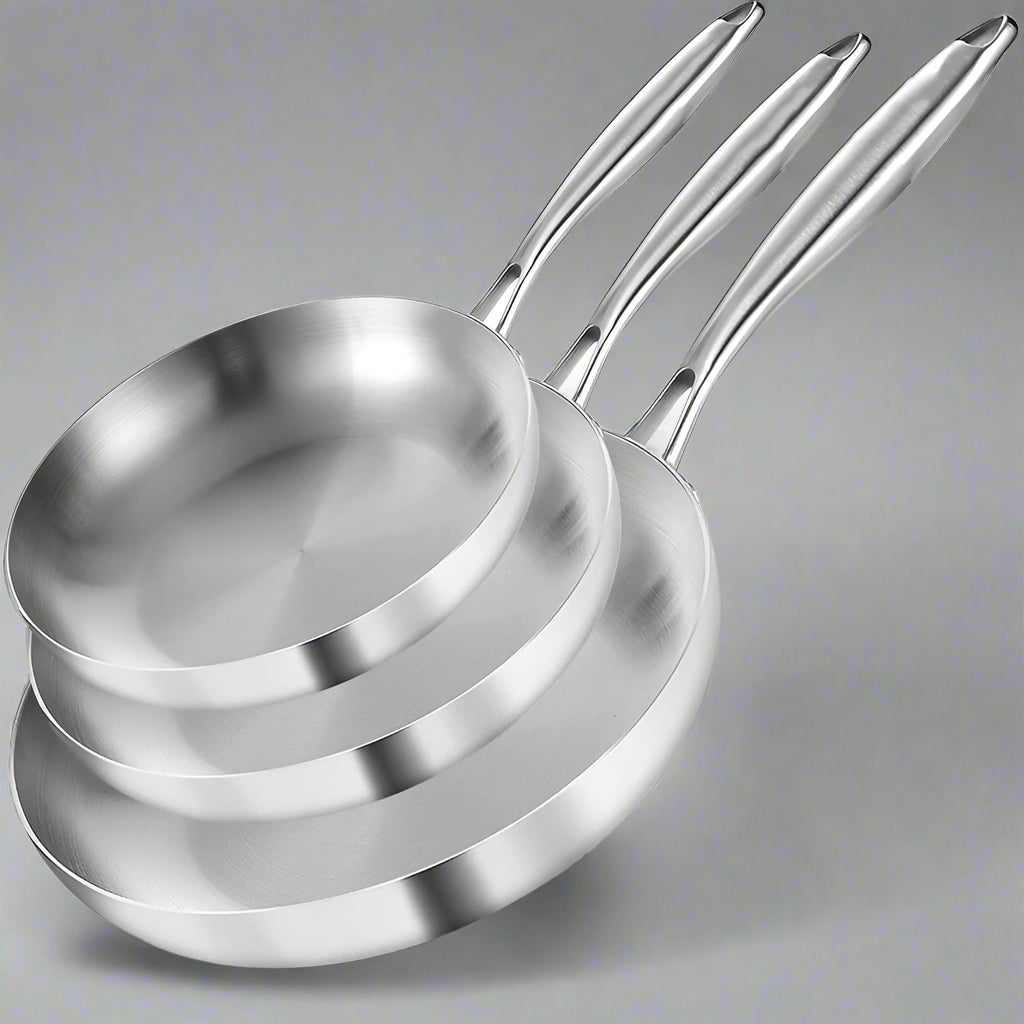 Set of three stainless steel frying pans with branding, accompanied by a steak and vegetables on a white background.
