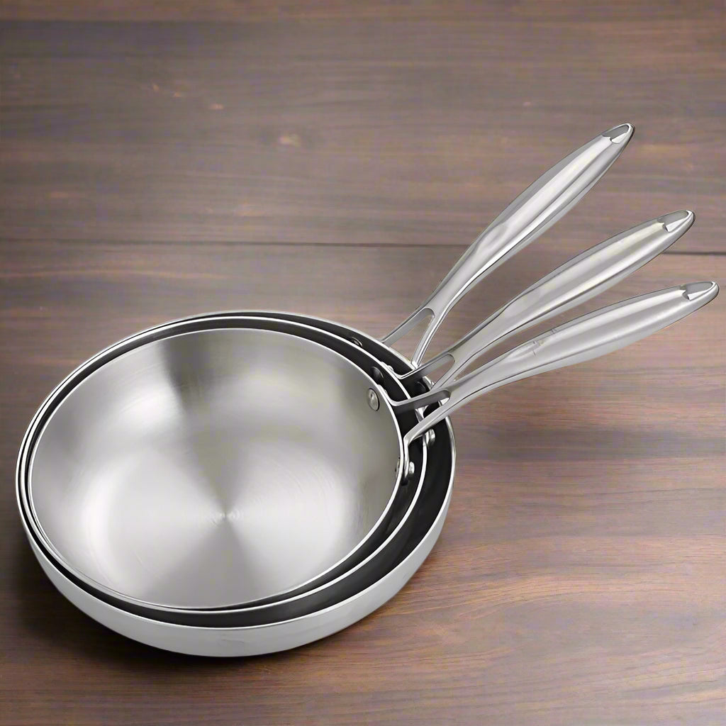 Set of stainless steel frying pans with food and vegetables on a white background