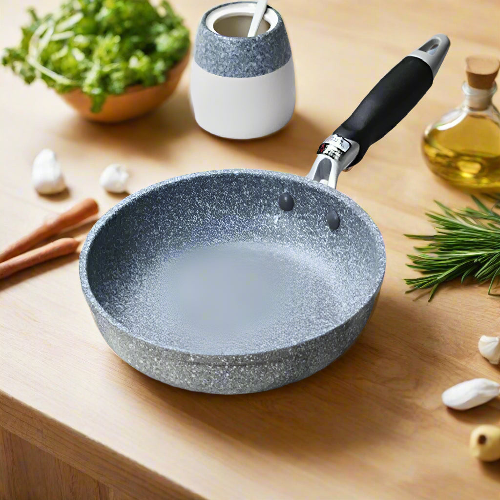 Gray speckled frying pan on a striped cloth with kitchen items around