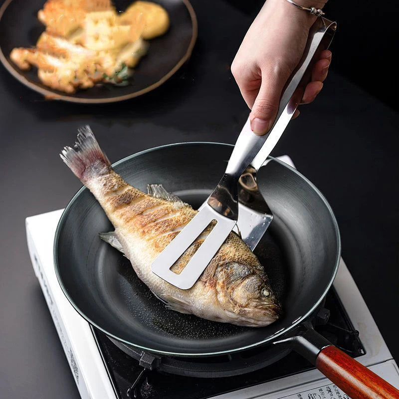 Person using a spatula to handle a fish in a frying pan on a stove.
