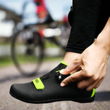 A person is adjusting the Velcro strap on a black cycling shoe with green accents, which is worn on a pedal of a bicycle.
