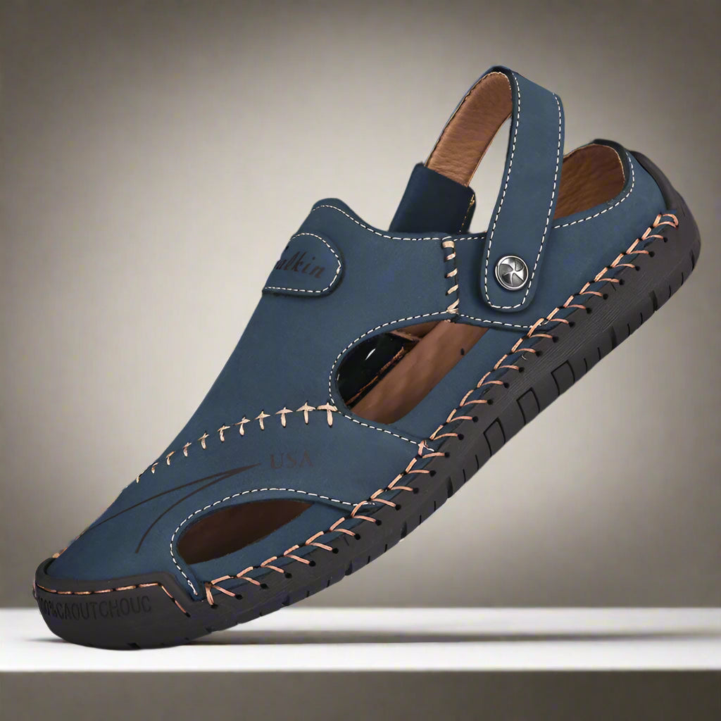 Blue sandal with brown stitching on a white stand against a black background