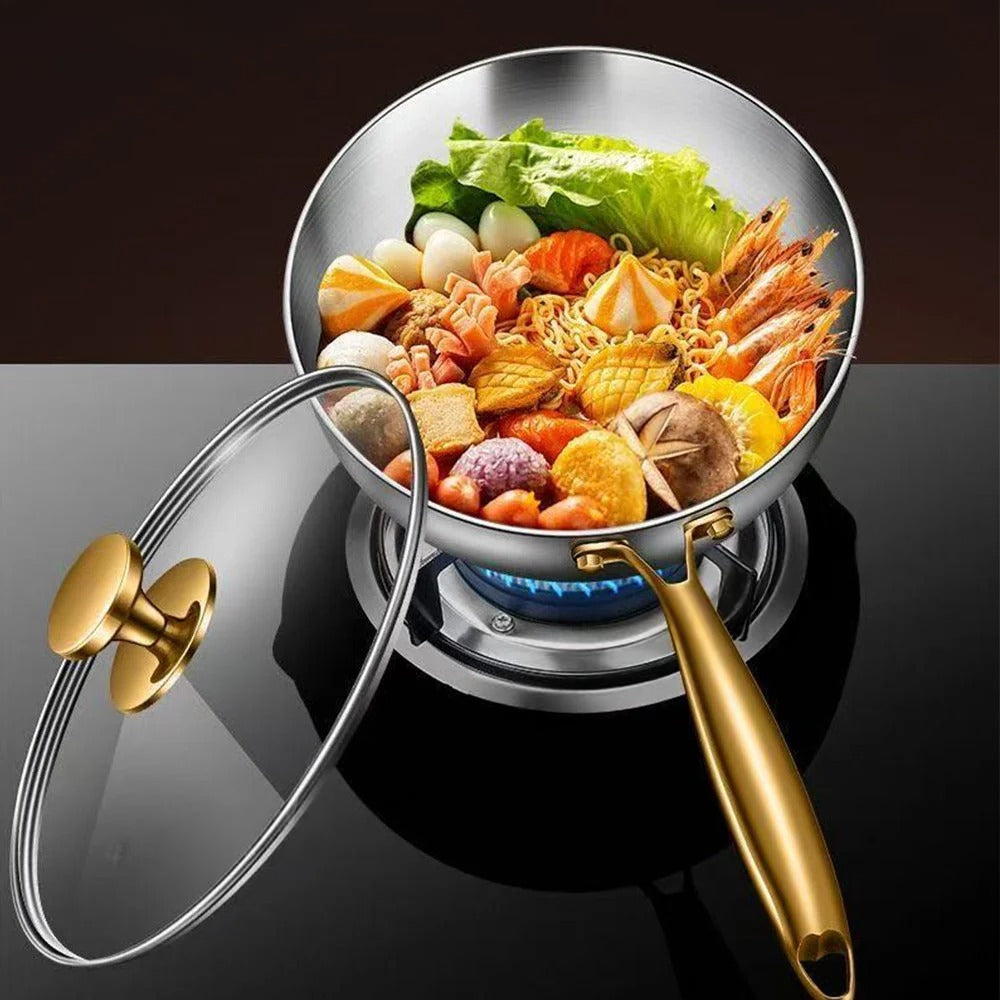 Stainless steel pot with gold handle and lid on a stove, filled with noodles and vegetables.