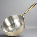 Stainless steel wok with a gold handle on a gray background