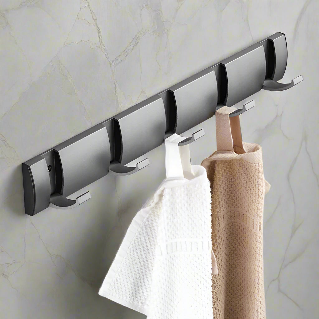 Wall-mounted hook rack with multiple hooks holding towels on a marble wall.
