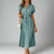 A woman wearing a green polka dot print button-up midi shirt dress with a natural waistline and short sleeves.