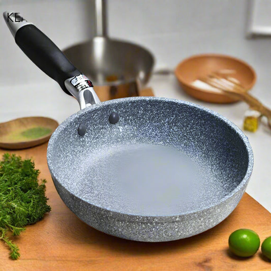 Gray speckled  stone frying pan on a wooden surface with a striped cloth underneath.