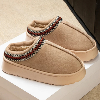 Pair of beige slippers with patterned straps on a white surface.