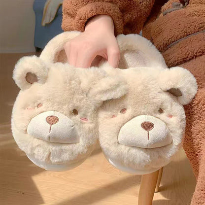 Pair of fluffy bear slippers held by a person wearing a brown outfit.
