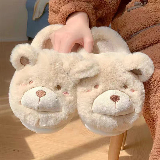 Pair of fluffy bear slippers held by a person wearing a brown outfit.