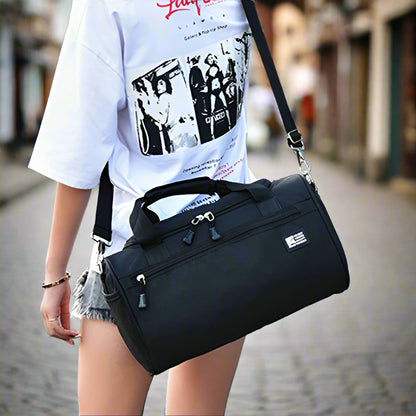 Person holding a black duffel bag in an outdoor setting