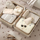 Open beige suitcase with organized packing including clothes, bags, and sunglasses on a patterned surface.