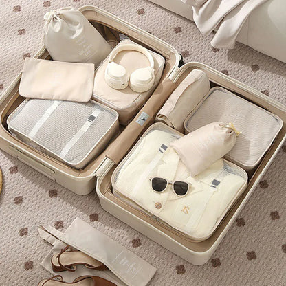 Open beige suitcase with organized packing including clothes, bags, and sunglasses on a patterned surface.