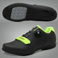 A person is adjusting the Velcro strap on a black cycling shoe with green accents, which is worn on a pedal of a bicycle.