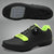A person is adjusting the Velcro strap on a black cycling shoe with green accents, which is worn on a pedal of a bicycle.
