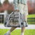 Person holding a gray pet carrier with a cat inside, outdoors.
