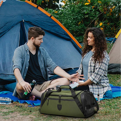 Two people sitting near a tent with a green duffel bag between them