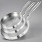 Set of three stainless steel frying pans with branding, accompanied by a steak and vegetables on a white background.