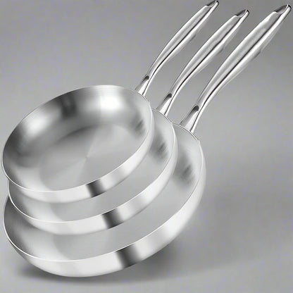 Set of three stainless steel frying pans with branding, accompanied by a steak and vegetables on a white background.