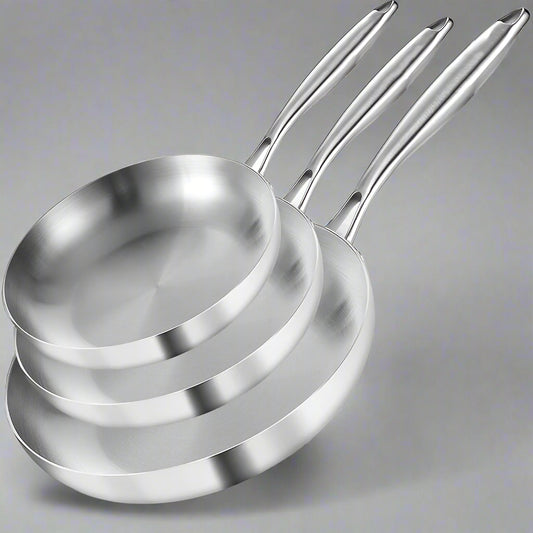 Set of three stainless steel frying pans with branding, accompanied by a steak and vegetables on a white background.