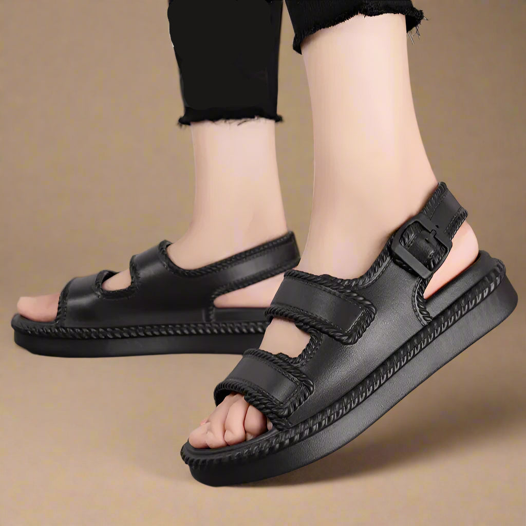 Black sandals worn by a person on a gray surface with text overlay.