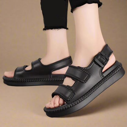 Black sandals worn by a person on a gray surface with text overlay.