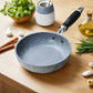 Gray speckled frying pan on a striped cloth with kitchen items around