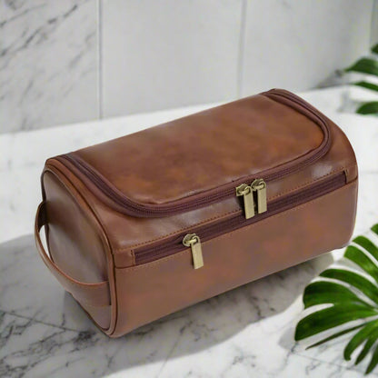Brown leather toiletry bag with gold zippers on a white background