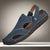 Blue sandal with brown stitching on a white stand against a black background