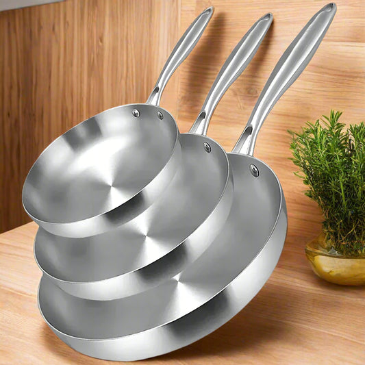 Set of three stainless steel frying pans stacked on a white background '' .