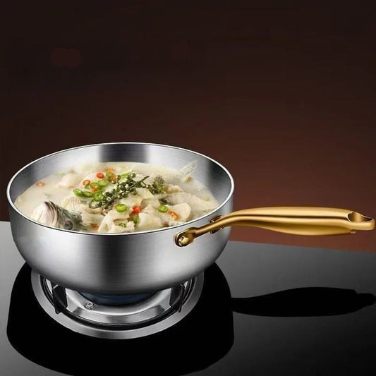 Stainless steel pot with gold handle containing a dish of food on a dark background
