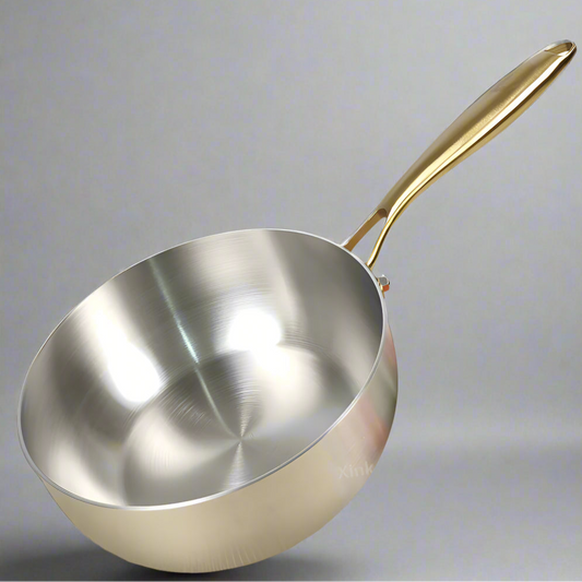 Stainless steel wok with a gold handle on a gray background