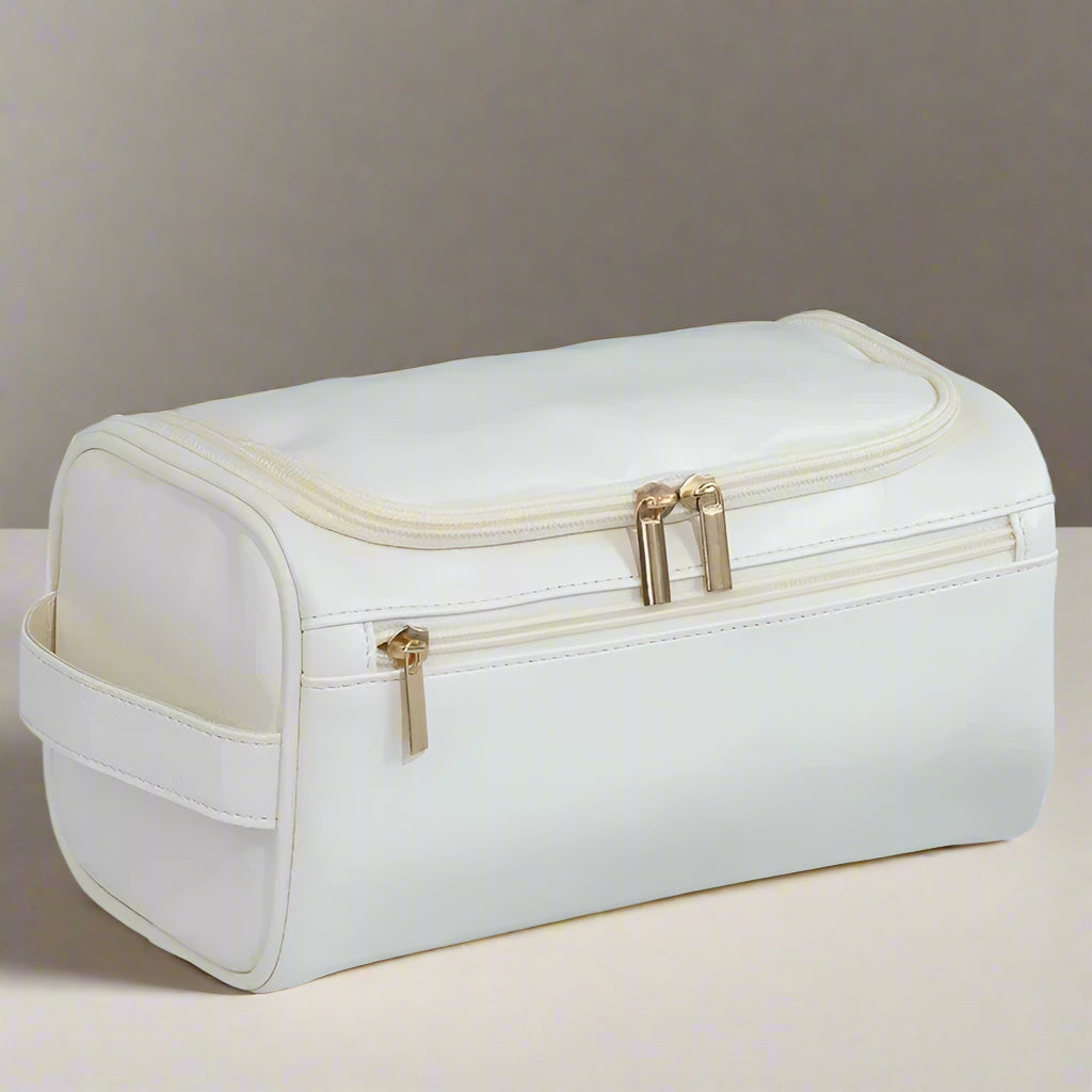 White toiletry bag with gold zippers on a light gray background